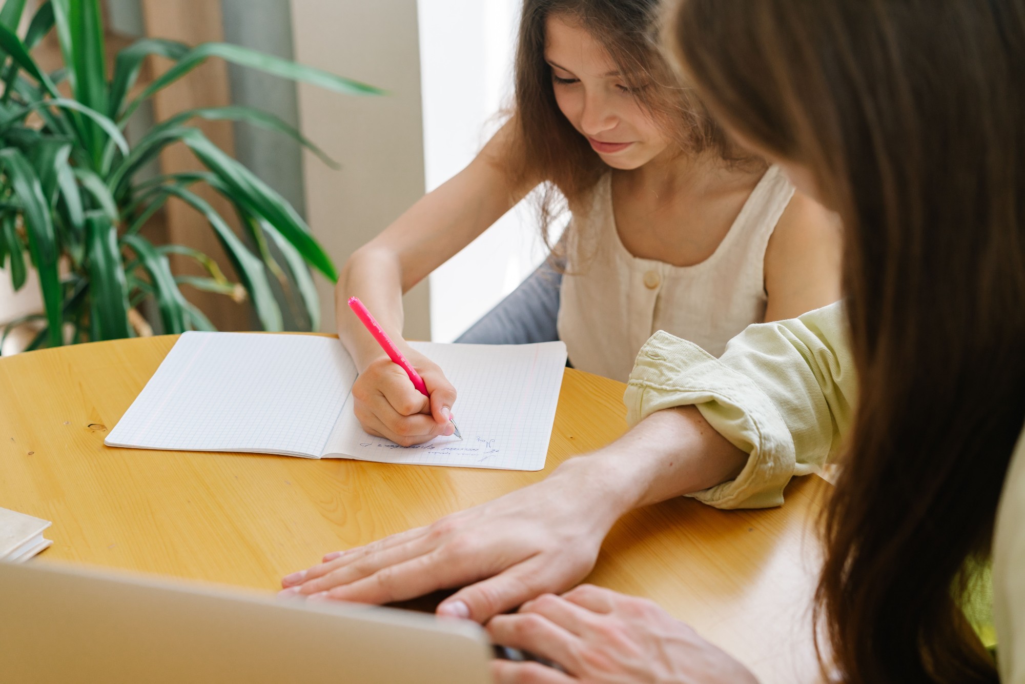 Mãe e filha sentadas à mesa, a jovem a escrever num caderno enquanto a mãe acompanha ao lado